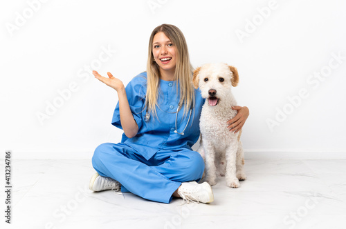 Young veterinarian woman with dog sitting on the floor extending hands to the side for inviting to come