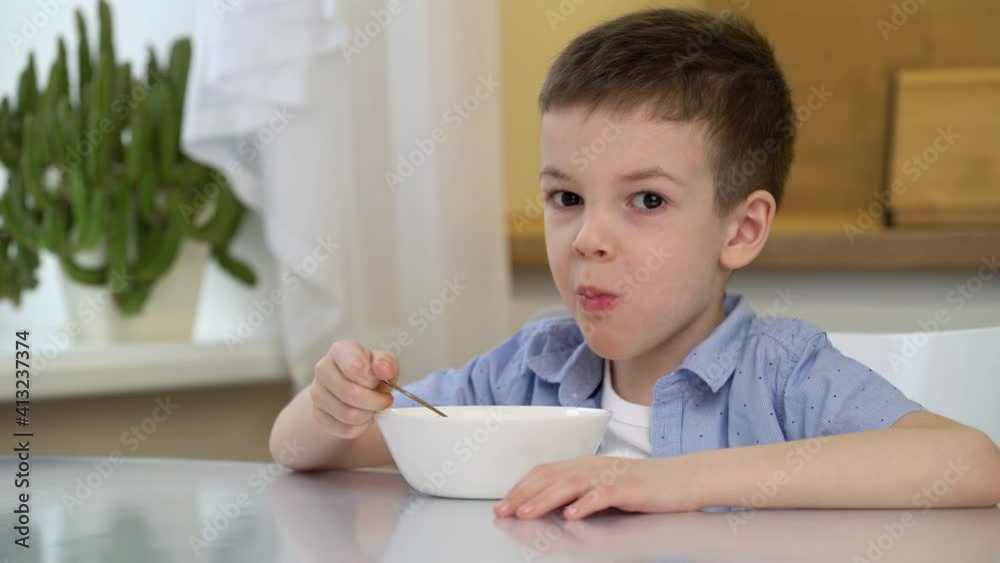 Small hungry boy eating tasting sweet corn flakes with milk at morning. Child boy sitting at kitchen table alone. Small hungry boy eating tasting sweet corn flakes with milk at morning. Child boy sitting at kitchen table alone.