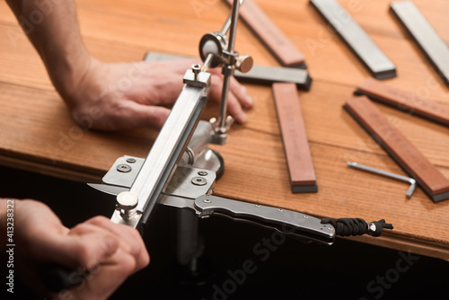 Close-up on man's hands using a manual machine to sharpen a folding knife