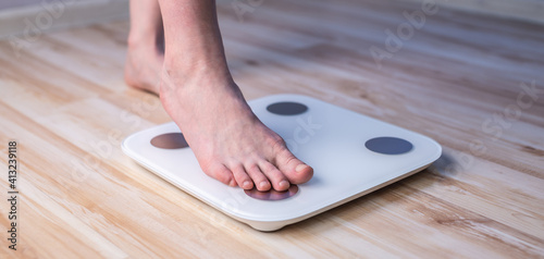 Women's bare feet stand on electronic scales on the wooden floor. Concept of fitness and weight loss tracking