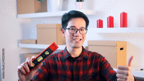 Young asian handyman showing thumb up and holding leveller in the other hand. High quality photo photo