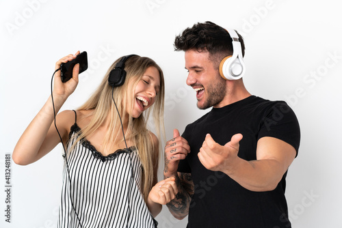 Young caucasian couple on white background listening music and dancing
