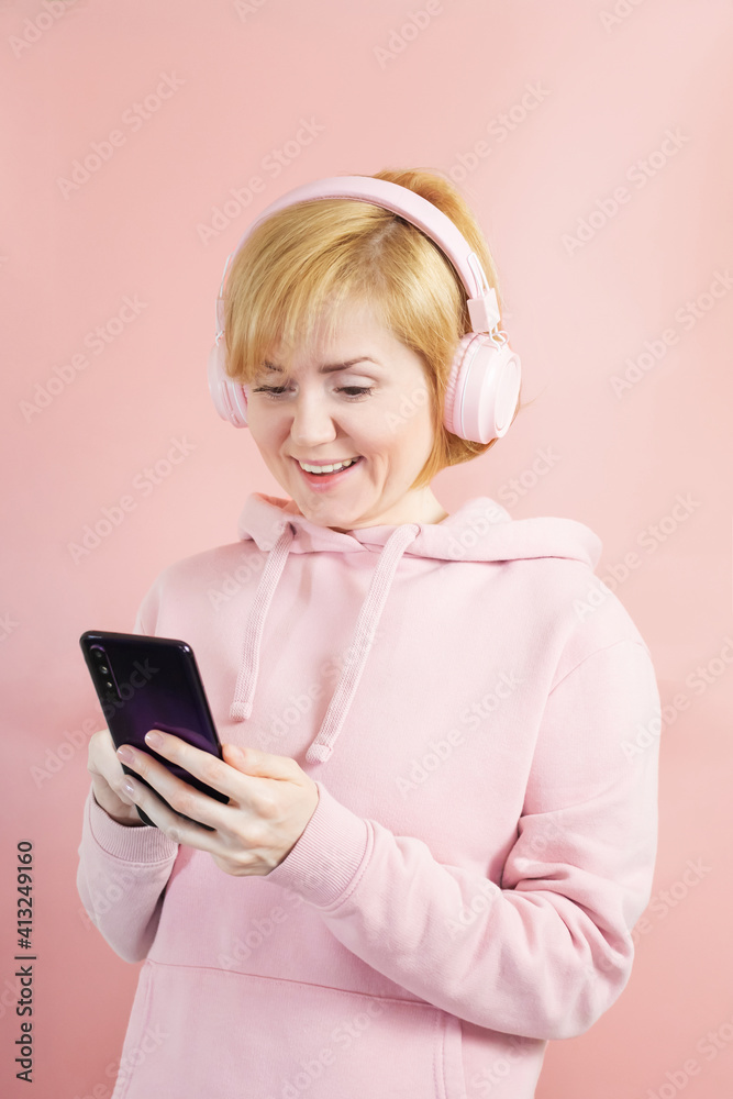 Caucasian girl in a pink sweatshirt and with pink headphones on a background similar in tone. Concept for music, podcasts, audiobooks. World Music Day, World Rock-n-roll Day. Caucasian girl in a pink sweatshirt and with pink headphones on a background similar in tone. Concept for music, podcasts, audiobooks. World Music Day, World Rock-n-roll Day.