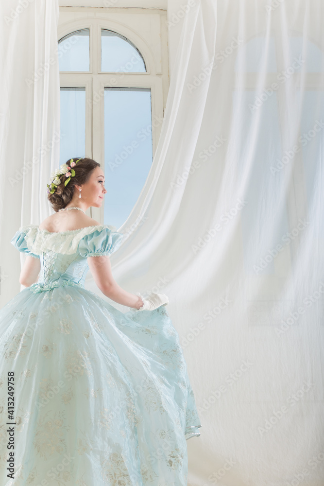 A beautiful elegant dark haired woman in a historic 1867 dress on background with window. High quality photo A beautiful elegant dark haired woman in a historic 1867 dress on background with window. High quality photo