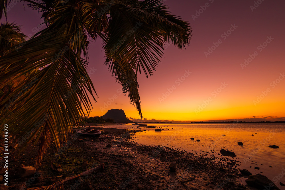Fishing boat and palm at sunset time. Le Morn mountain in Mauritius.