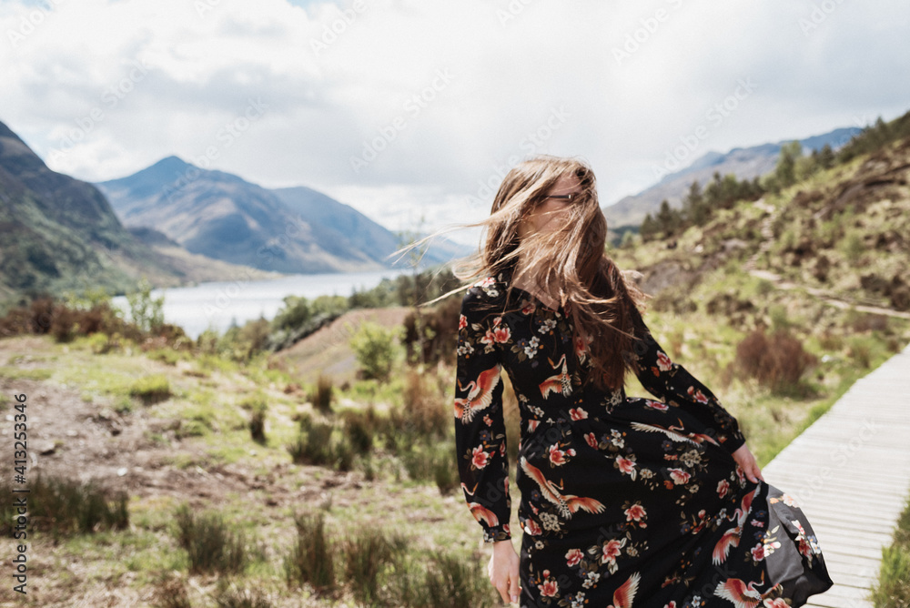 Frau mit Kleid und wehenden Haaren vor dem Gesicht in einer schottischen Landschaft mit Bergen und See im Hintergrund