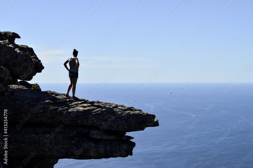 A girl standing on a rock on the top of a mountain enjoying the view of the sea, in Kasteelspoort hike. Cape Town, South Africa.