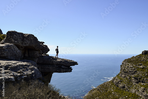 A girl standing on a rock on the top of a mountain in Kasteelspoort hike. She is enjoying the view of the sea and the city. Cape Town, South Africa.