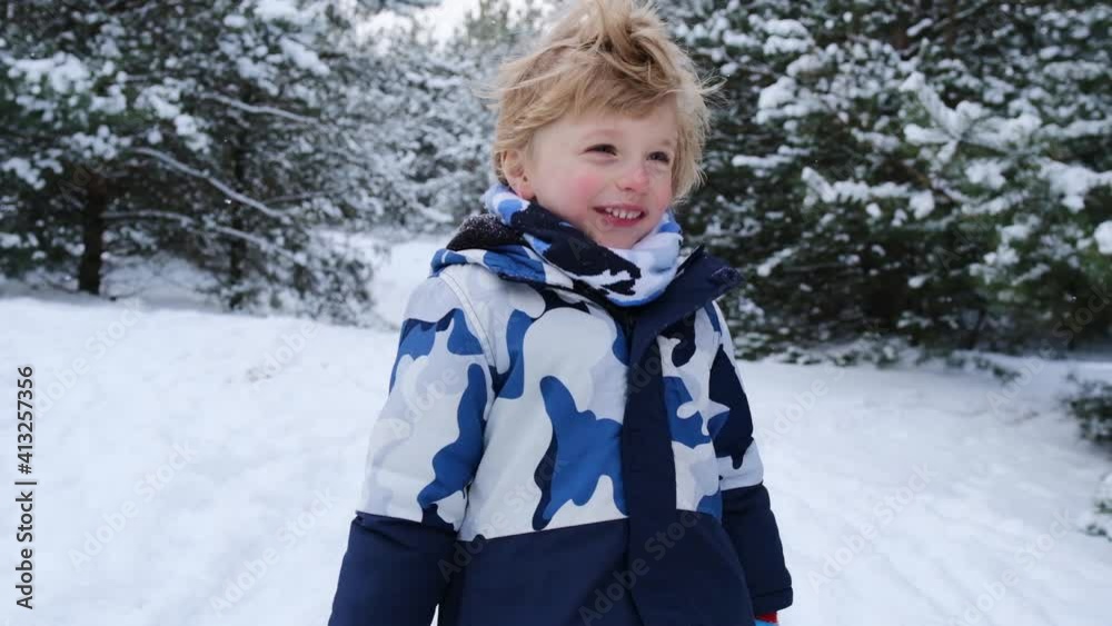 Cute positive young boy with tousled blonde hair enjoying winter looking at camera with toothy smile, playing and running in snow, having fun, childhood, slow motion Cute positive young boy with tousled blonde hair enjoying winter looking at camera with toothy smile, playing and running in snow, having fun, childhood, slow motion