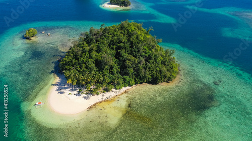 Island with a sandy beach and azure water surrounded by a coral reef and an atoll. Britania Islands, Surigao del Sur, Philippines.