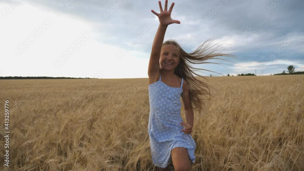Close up of happy girl with long blonde hair running to the camera through barley field. Little smiling kid jogging over the wheat meadow. Cute child spending time at golden plantation. Slow motion