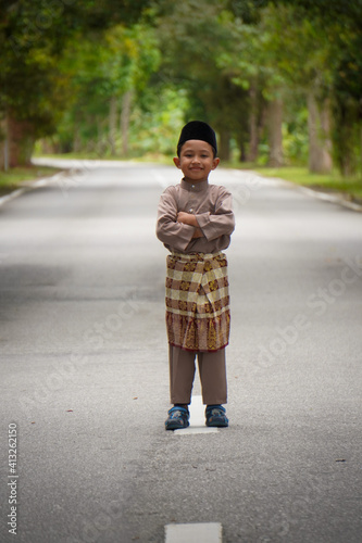 A Malay boy in Malay traditional cloth showing his happy reaction during Eid Fitri or Hari Raya celebration.