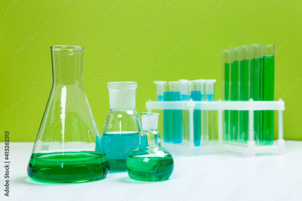 Various laboratory glass items with water and empty on white table with green background Various laboratory glass items with water and empty on white table with green background