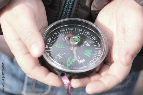 Old classic navigation compass in childs hands on natural background as symbol of tourism with compass, travel with compass and outdoor activities with compass