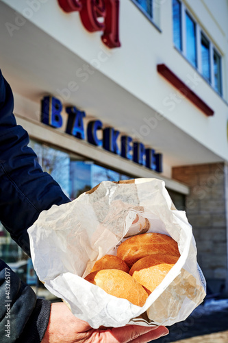 View into an open paper bag with fresh buns that is held in hands. The unfocussed blue text on the house wall is German for bakery.