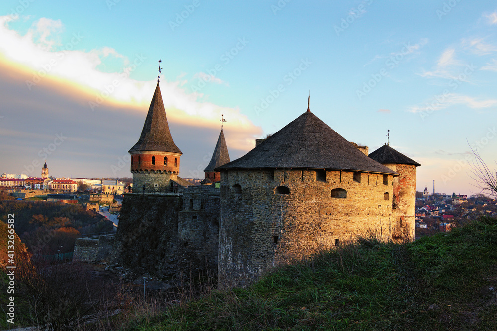 Scenic landscape photo of ancient stone fortress in the city of Kamianets-Podilskyi during winter sunset. Panoramic dramatic sunset sky. Famous touristic place and romantic travel destination. Ukraine