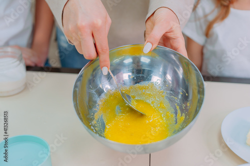 Mom teaches her daughters to make dough in the kitchen and beat eggs.