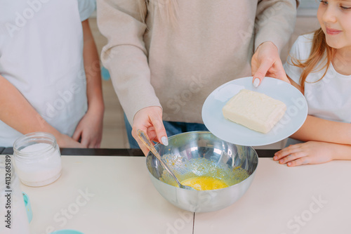 Mom teaches her daughters to make dough in the kitchen and beat eggs.