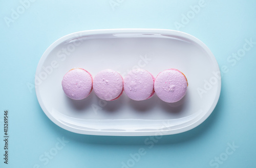 French macaroni cakes in pink on a white oval plate on a blue background.