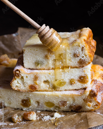 Close-up of cottage cheese casserole with raisins and honey on a baking paper on a wooden table. Russian traditional dessert zapekanka photo