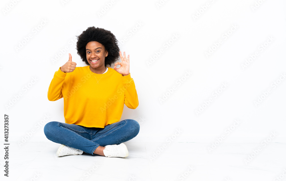 Young African American woman sitting on the floor showing ok sign and thumb up gesture Young African American woman sitting on the floor showing ok sign and thumb up gesture