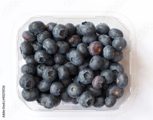 Plastic punnet full of lush blueberries against plain white background