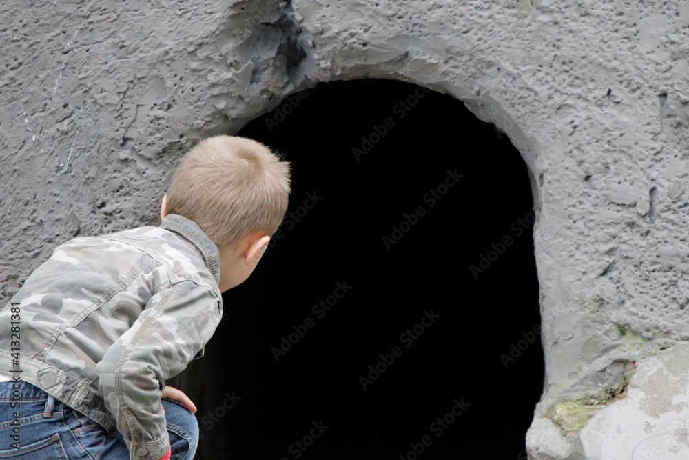 The child looks into the black hole of the cave. The concept of learning the unknown. Childish curiosity. The child looks into the black hole of the cave. The concept of learning the unknown. Childish curiosity.