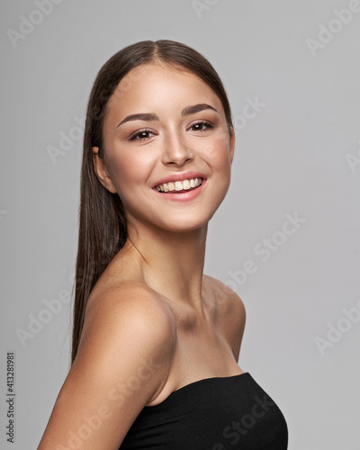 Young beautiful female model close-up studio beauty portrait. Girl with natural make-up and long brunette straight hair. Happy smiling woman looking at you