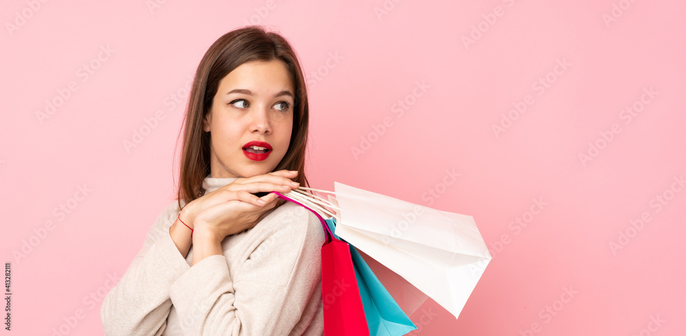 Teenager girl isolated on pink background holding shopping bags and looking back Teenager girl isolated on pink background holding shopping bags and looking back