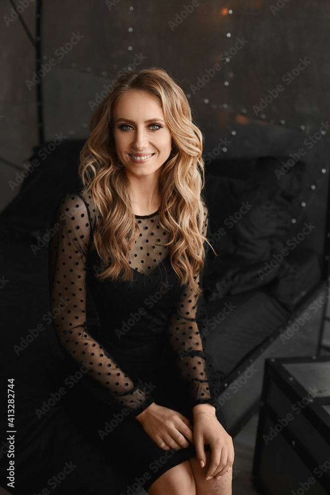 Young model woman with evening makeup in a black cocktail dress smiling and posing indoors Young model woman with evening makeup in a black cocktail dress smiling and posing indoors