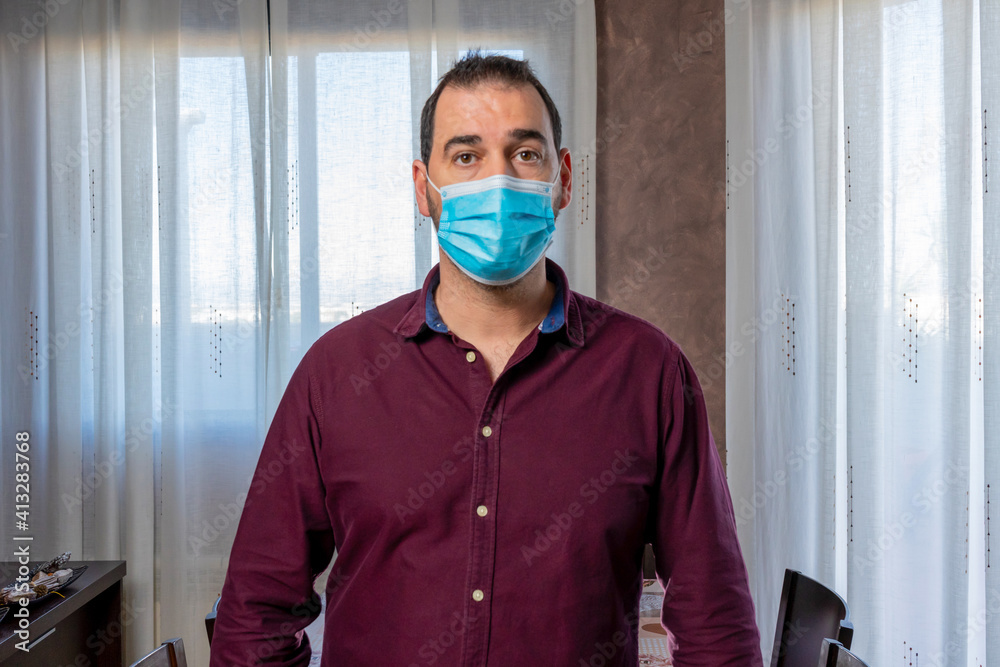 Handsome bearded man in a purple shirt posing with a surgical mask to protect himself from coronavirus Handsome bearded man in a purple shirt posing with a surgical mask to protect himself from coronavirus