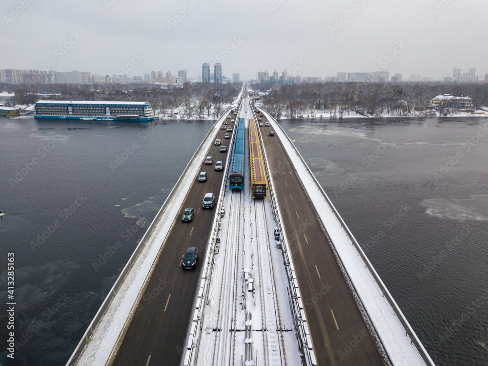 Two metro trains on a snow-covered metro bridge in Kiev. Cloudy winter morning. Aerial drone view.