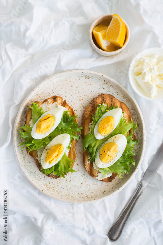 Two egg's sandwiches with cream cheese, green salad and lemon on the white plate, on light background.