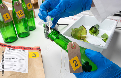 Police expert gets blood sample from a green glass bottle in Criminalistic Lab, conceptual image photo