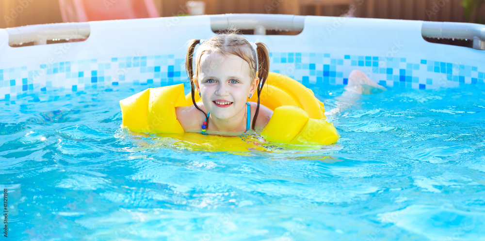 Little girl is splashing in iswimming pool outdoor, having fun.