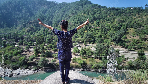 Back view of a girl with thands up standing on a stone in the high mountains - success concept photo