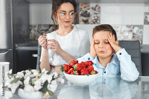 A sad boy sits at the table and looks at a plate with strawberries. Food allergy.
