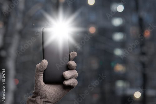 Gloved hand holds a smartphone with a burning flashlight with lighting windows of Moscow dwelling house on the background. Political flash mob. Copy space. photo