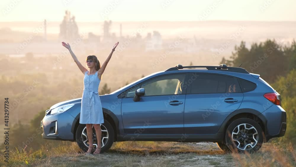 Young female driver resting near her car raising up her hands on warm summer evening. Travel destinations concept. Young female driver resting near her car raising up her hands on warm summer evening. Travel destinations concept.