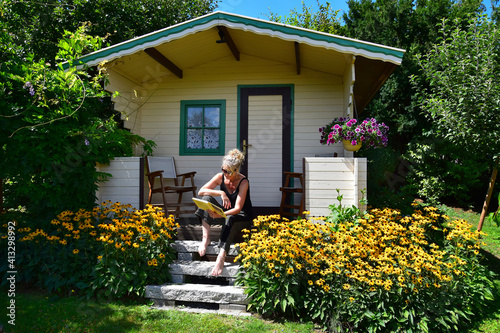 A woman sitting on the stairs of a garden shed, reading a book.