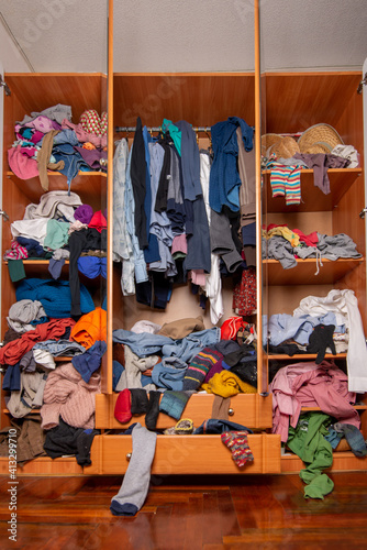 Huge closet filled with used clothes, sloppily shoved and hanging from shelves and hangers. Wardrobe mess