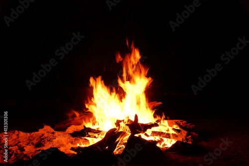 Bright flames, embers, and burning wood illuminating the ground around a camp fire.