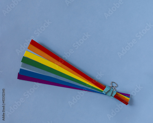 Rainbow bouquet. Strips of rainbow colored paper are held together with a paper clip. Light blue background. 