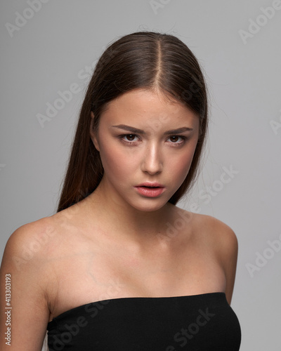 Young beautiful female model close-up studio beauty portrait. Girl with natural make-up and long brunette straight hair. Calm woman looking at you