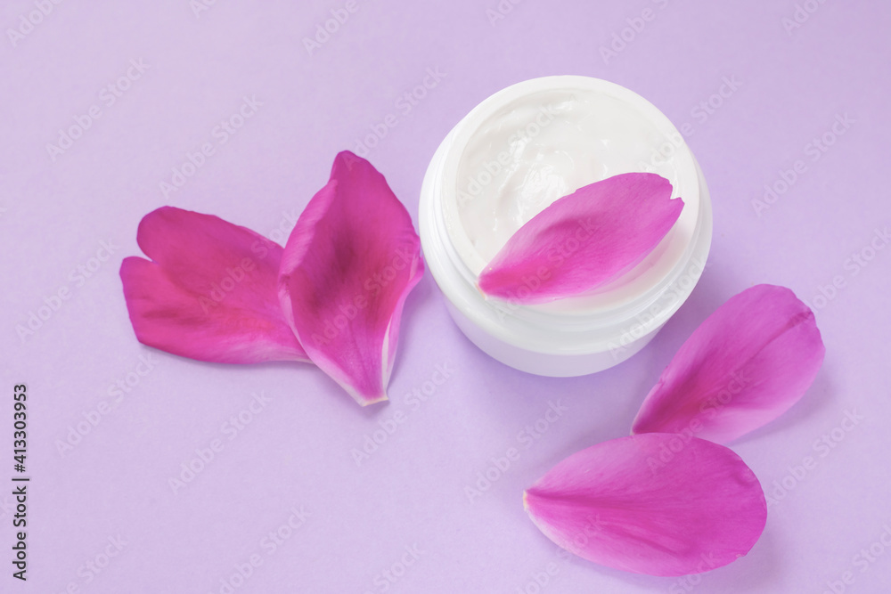 Toned soft photo of container with white cream with peony oil essential or extract and petals on pink background Toned soft photo of container with white cream with peony oil essential or extract and petals on pink background