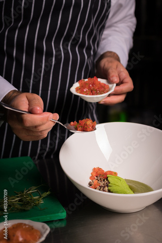 Chef cook preparing salad with salmon and avocado in his kitchen. Freezer food prepare in process vegetarian salad by chef hand in home kitchen. Dark black background with Text area for design menu 