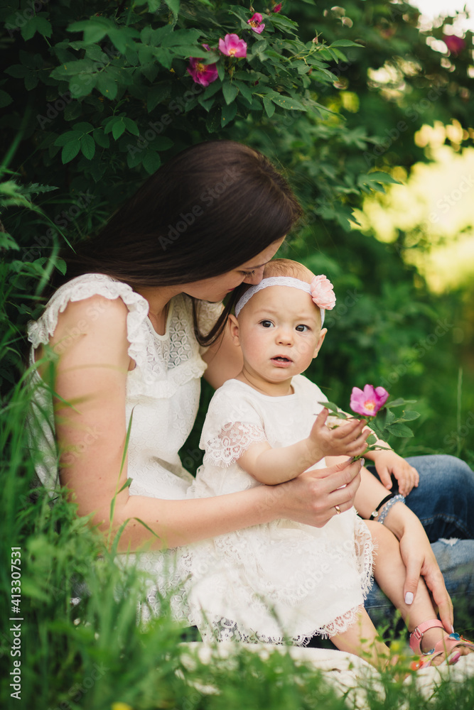 Mother and child daughter in spring garden. Young woman and baby girl together standing near the blooming bush with pink rose flowers. Baby touching flowers on bush. summer time Mother and child daughter in spring garden. Young woman and baby girl together standing near the blooming bush with pink rose flowers. Baby touching flowers on bush. summer time