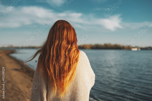 Back view of a woman with long ginger hair walking outdoors in sunlight enjoying nature.