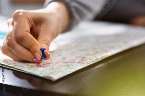 Female hand holding pushpin showing the location of a destination point on a map. Travel destination, pin on the map. Selective focus. Blue pushpin, map on table