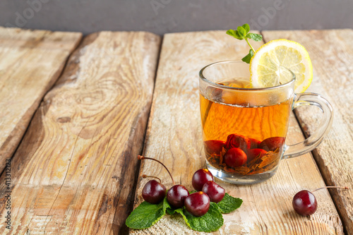 black tea with mint cherries and lemon on a wooden table next to fresh cherries.